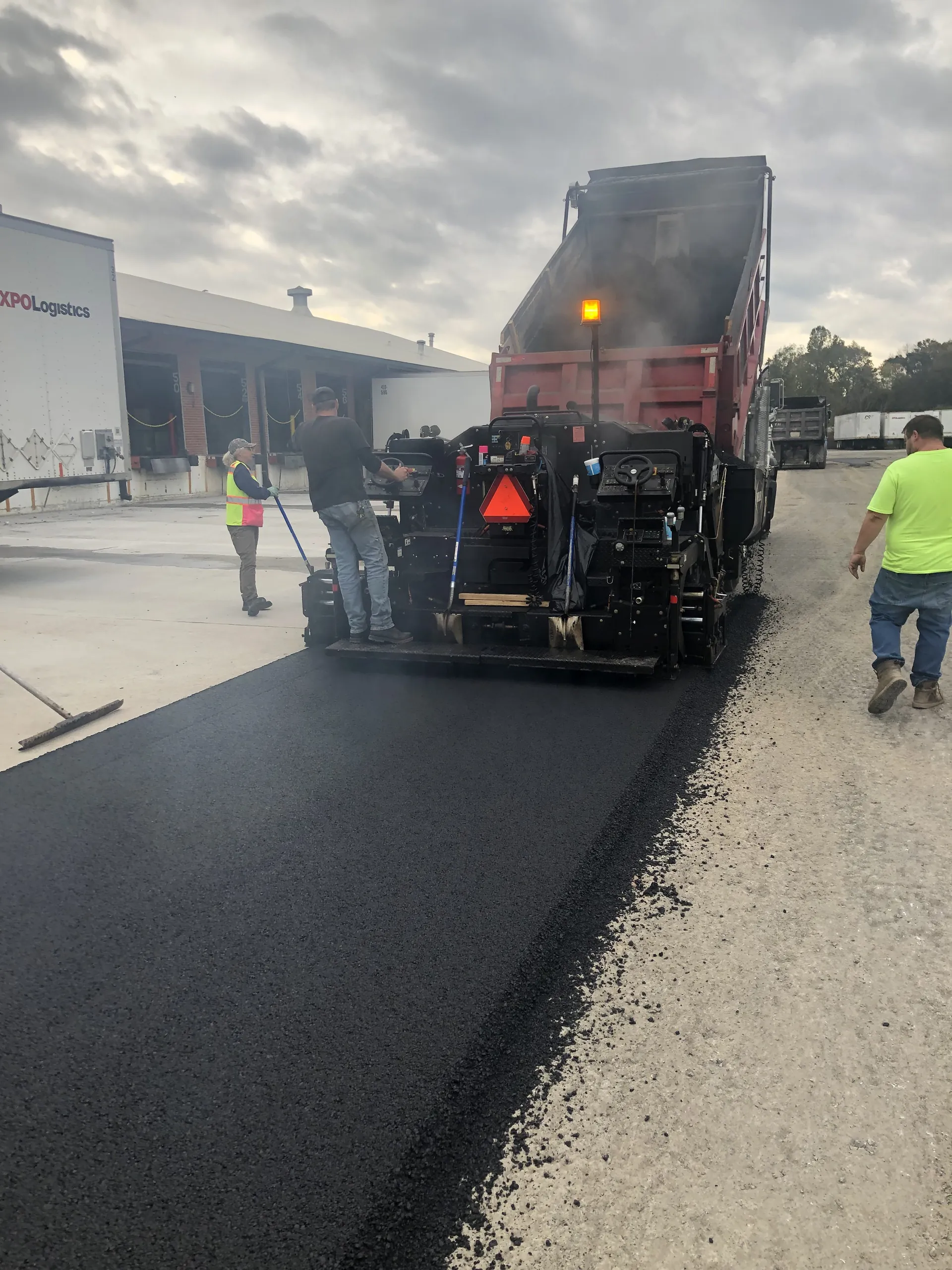 Project One Contracting crew operating an asphalt paver to lay fresh hot mix at the XPO Logistics loading dock