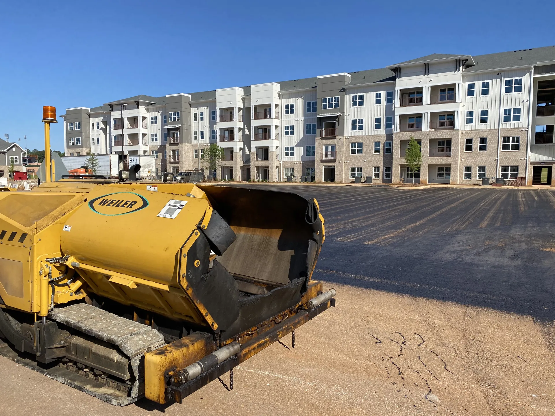 Weiler material transfer paver staged on a freshly paved multifamily apartment parking lot built by Project One Contracting