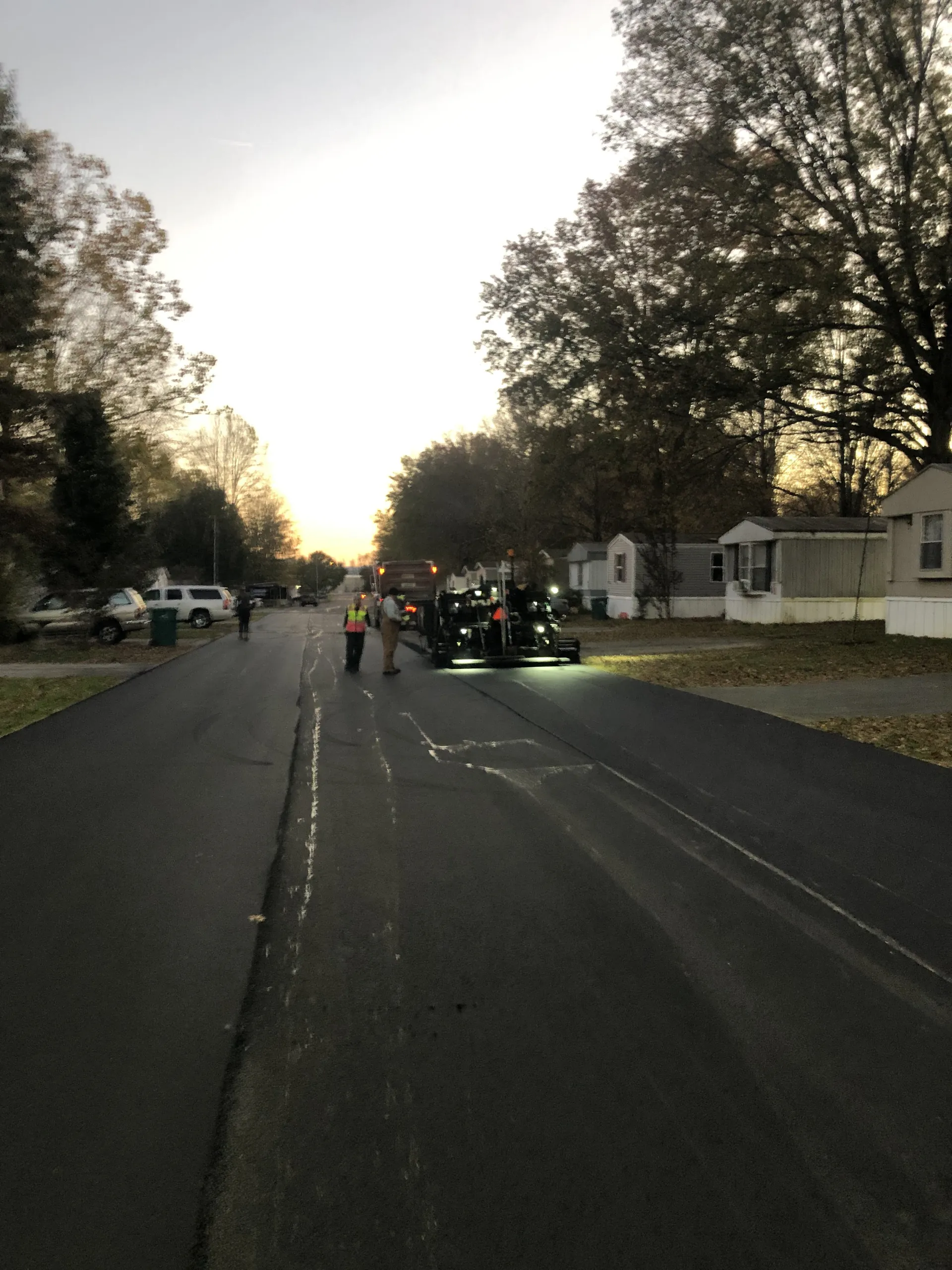 Asphalt paver and crew laying down hot mix at sunset