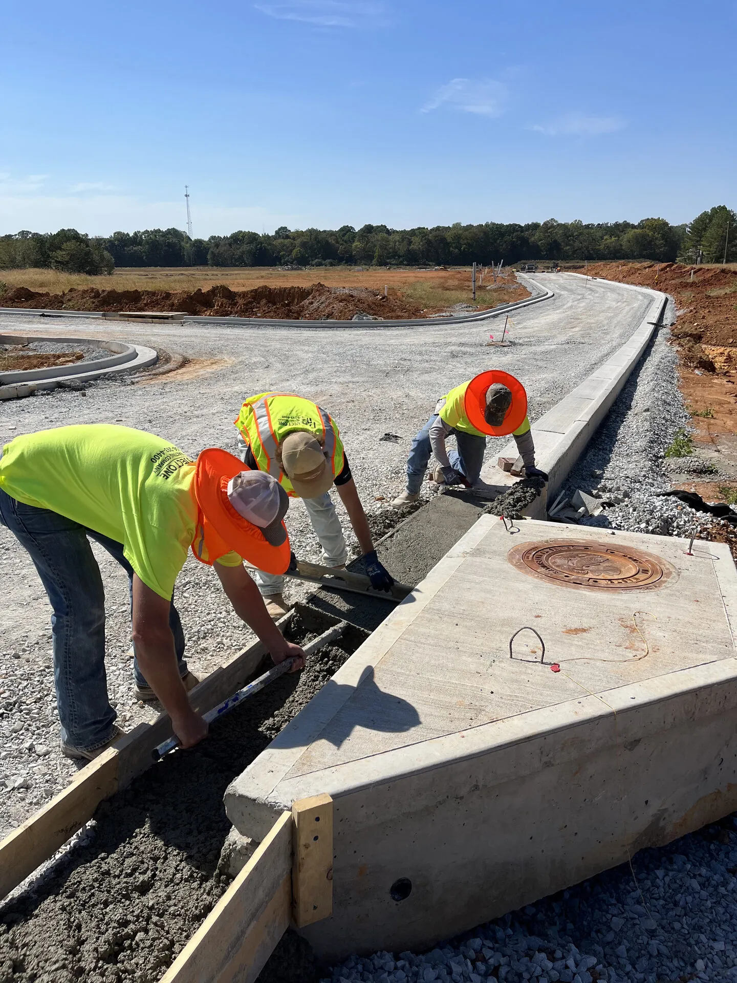 Project One Contracting crew hand-finishing a poured concrete curb beside a freshly graded commercial driveway in North Alabama