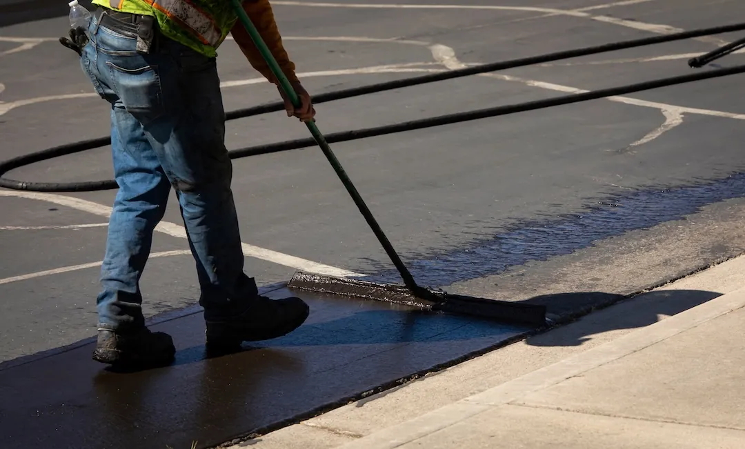 Crew applying sealcoat to an asphalt driveway with a brush